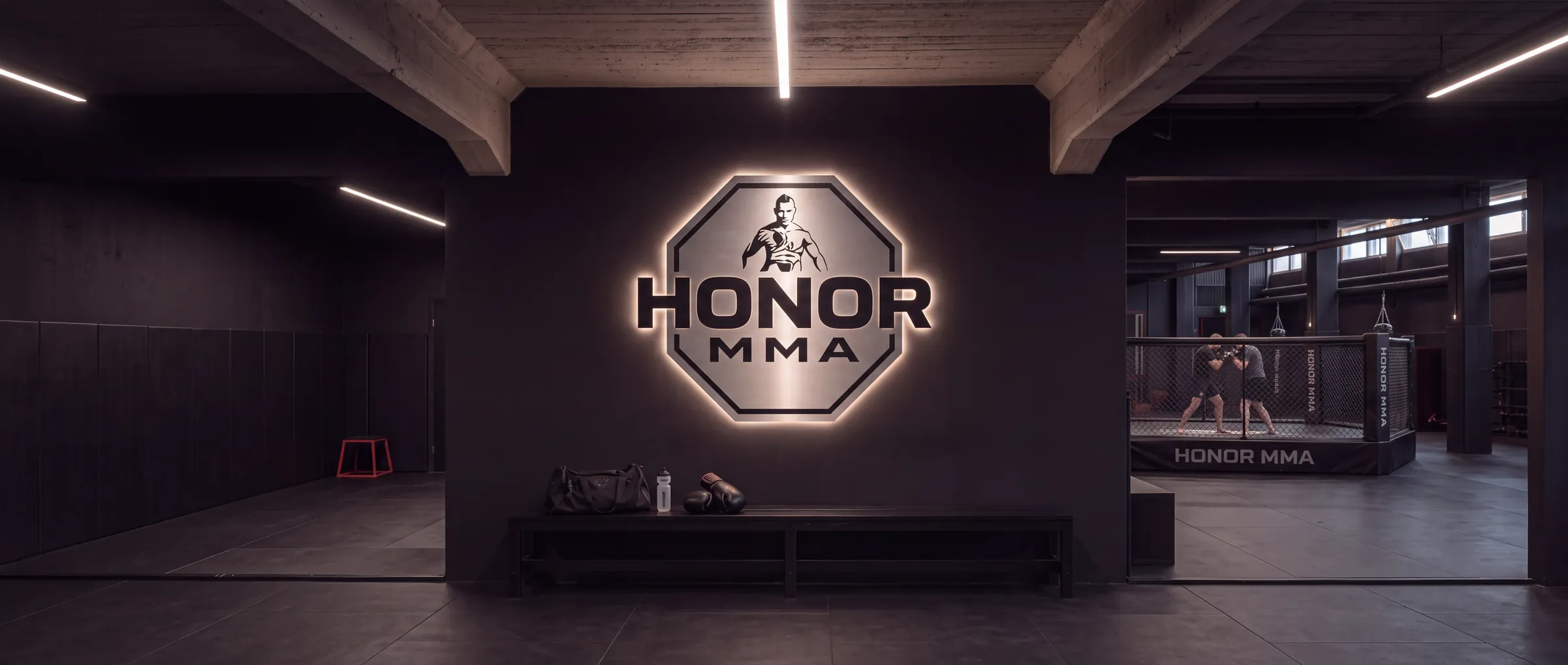 Eingangsbereich mit beleuchtetem HONOR-MMA-Emblem, Bank und Blick in die Halle
